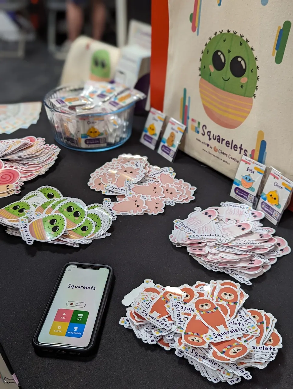 Photo of the Squarelets stand at Indieverse during Insomnia #i71: we had stickers pins, totes and a few phones to play on